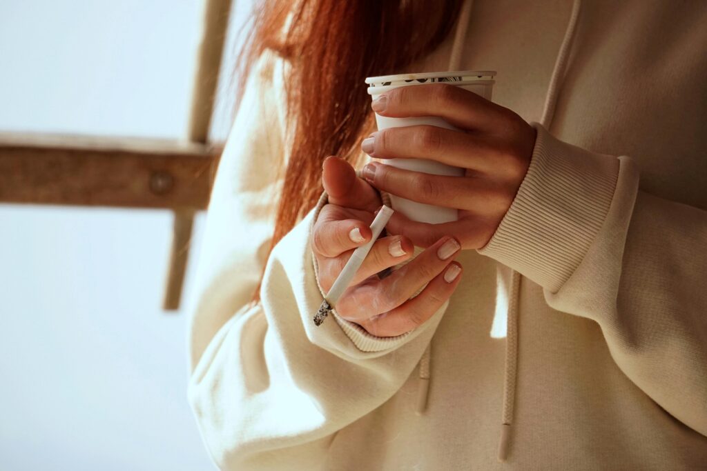 Close-up of a woman holding a coffee cup and cigarette in natural light.